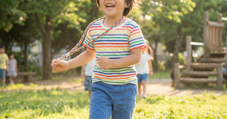 晴れた公園で首からストラップを下げて走る元気な子供。