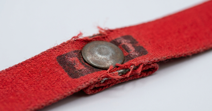 金属製のカシメが物理的にロゴの上に重なってしまい、ロゴが隠れているネックストラップの失敗例